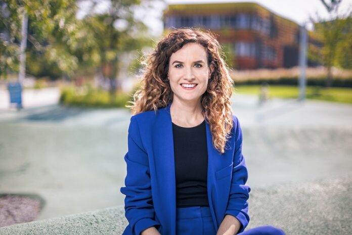 Judith Kohlenberger © Markus Zahradnik Das Bild zeigt Judith Kohlenberger. Sie trägt einen blitzblauen Anzug und ein schwarzes Shirt. Ihre Haare sind brünett, lang und lockig. Sie sitze auf einer Mauer und lächelt freundlich in die Kamera.