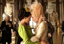 „Court Life” / Kulturforum London Das Bild zeigt eine Szene des Films „Farewell my Queen“. Marie Antoinette trägt ein hell goldenes Kleid und steht Stirn an Stirn mit ihrer Dame Sidonie Laborde, die ein grünes Kleid trägt.