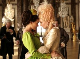 „Court Life” / Kulturforum London Das Bild zeigt eine Szene des Films „Farewell my Queen“. Marie Antoinette trägt ein hell goldenes Kleid und steht Stirn an Stirn mit ihrer Dame Sidonie Laborde, die ein grünes Kleid trägt.
