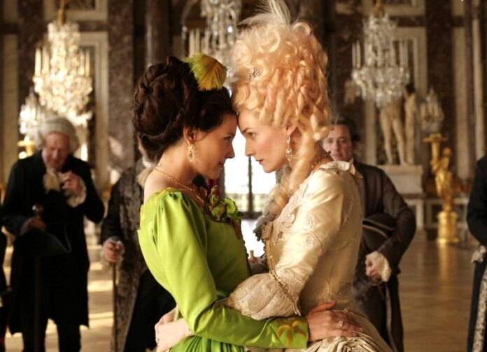 Das Bild zeigt eine Szene des Films „Farewell my Queen“. Marie Antoinette trägt ein hell goldenes Kleid und steht Stirn an Stirn mit ihrer Dame Sidonie Laborde, die ein grünes Kleid trägt.