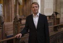 Orgelklänge am Bosporus / Kulturforum Istanbul Das Bild zeigt Stefan Donner in dunklem Anzug, der lächelnd in einem Kirchenraum mit hölzernen Sitzbänken steht und in die Kamera blickt.