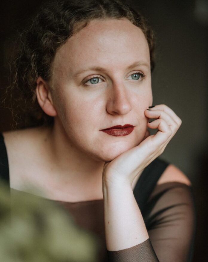 Auf dem Bild sieht man die Autorin in Nahaufnahme, sie blickt verträumt in die Ferne und stützt den Kopf auf die Hand.