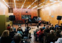 BUNT Festival 2025 / Kulturforum Belgrad Das Bild zeigt ein holzverkleidetes Tonstudio, in dem ein Saxophonist und eine Pianistin am Klavier vor einem sitzenden Publikum zwischen Mikrofonen und Lautsprechern auftreten.