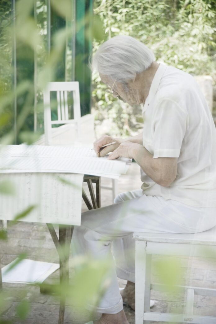 Das Bild zeigt einen alten Mann in einem Garten sitzend über eine Partitur gebeugt