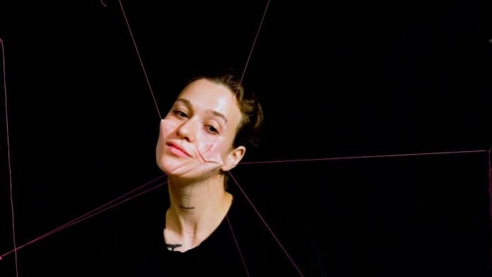 1) Das Bild zeigt die Künstlerin, der Haut im Gesicht an rote Fäden geknüpft ist, die diese in mehrere Richtungen ziehen und somit das Gesicht entstellen.