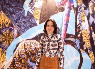 Sunny Pfalzer – Cripto Sirenas / Kulturforum Ottawa Das Bild zeigt die österreichische Künstlerin Sunny Pfalzer, die vor einem ihrer Kunstwerke steht und lächelt.