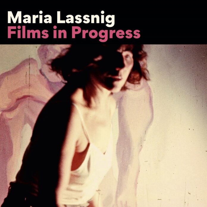 Das Bild zeigt eine verschwommene Person vor einer abstrakten Projektion in sanften Farben. Sie trägt ein weißes Top und scheint in Bewegung zu sein. Der Titel „Maria Lassnig: Films in Progress“ ist oben in moderner Schrift zu sehen.