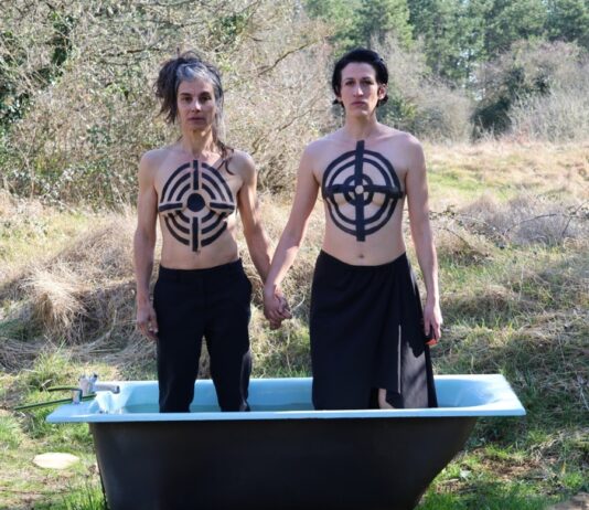Why „We Should All Be Feminists”/ Kulturforum Zagreb Das Bild zeigt zwei nackte Frauen mit aufgemalten Zielscheiben auf ihren Körpern, die händehaltend in einer Badewanne in der Natur stehen