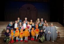 Klangdialog Österreich – Mongolei / Kulturforum Peking Gruppenfoto auf einer Theaterbühne nach einer Opernaufführung. In der Mitte steht der Dirigent Matthias Fletzberger in Frack, umgeben von Sängerinnen, Sängern und Darstellern in aufwendigen, farbenfrohen Kostümen, darunter auch mehrere Kinder in vogelähnlichen Bühnenoutfits. Die Mitwirkenden halten Blumen und blicken lächelnd in die Kamera..