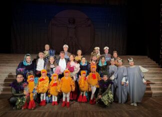 Klangdialog Österreich – Mongolei / Kulturforum Peking Gruppenfoto auf einer Theaterbühne nach einer Opernaufführung. In der Mitte steht der Dirigent Matthias Fletzberger in Frack, umgeben von Sängerinnen, Sängern und Darstellern in aufwendigen, farbenfrohen Kostümen, darunter auch mehrere Kinder in vogelähnlichen Bühnenoutfits. Die Mitwirkenden halten Blumen und blicken lächelnd in die Kamera..