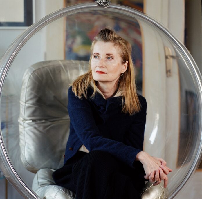 Man sieht Elfriede Jelinek, sie sitzt in einem durchsichtigen Schwingsessel und blickt in die Ferne. elfriede jelinek in ihrem haus 1140 wien bubble chair von aarnio eero