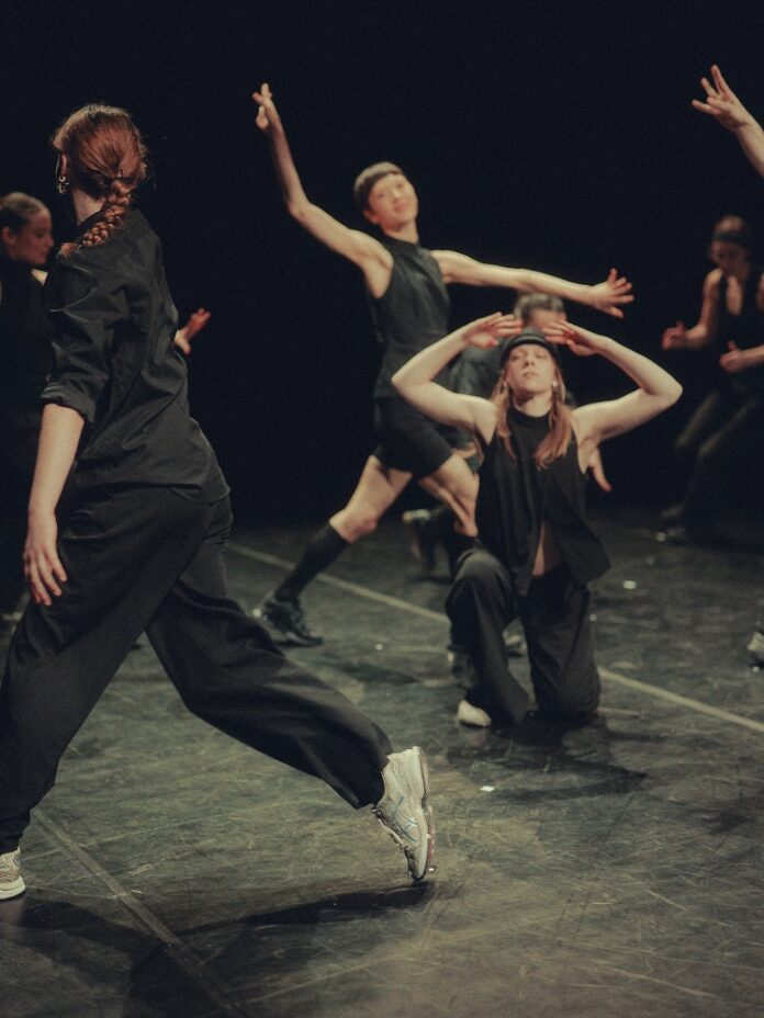 Das Bild zeigt Tänzerinnen und Tänzer während einer Probe, schwarz gekleidet