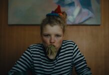 Film von Florian Pochlatko / Kulturforum Prag Das Bild zeigt eine junge Frau mit vollem Mund voller Spaghetti, die an einem Esstisch sitzt und in die Kamera starrt.