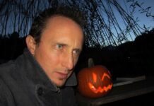 Autor Christian Kössler in Riga / Botschaft für Lettland Das Bild zeigt Christian Kössler, der draußen in der Dämmerung neben einem leuchtenden Halloween-Kürbis sitzt.