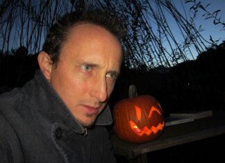 Autor Christian Kössler in Riga / Botschaft für Lettland Das Bild zeigt Christian Kössler, der draußen in der Dämmerung neben einem leuchtenden Halloween-Kürbis sitzt.