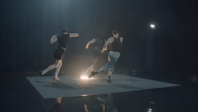 Das Bild zeigt drei Tänzer:innen auf der Bühne in Bewegung