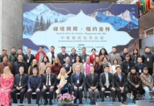 Ausstellung / Kulturforum Peking Das Bild zeigt ein Gruppenfoto der beteiligten Künstlerinnen, Künstler und Gäste bei der Ausstellung „Gipfeltreffen der Künste – Begegnung mit Jilin“. Die Gruppe ist vor dem Ausstellungsplakat mit Bergmotiv und chinesischer Schrift auf einer Bühne versammelt.