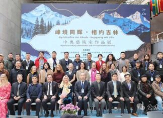 Ausstellung / Kulturforum Peking Das Bild zeigt ein Gruppenfoto der beteiligten Künstlerinnen, Künstler und Gäste bei der Ausstellung „Gipfeltreffen der Künste – Begegnung mit Jilin“. Die Gruppe ist vor dem Ausstellungsplakat mit Bergmotiv und chinesischer Schrift auf einer Bühne versammelt.