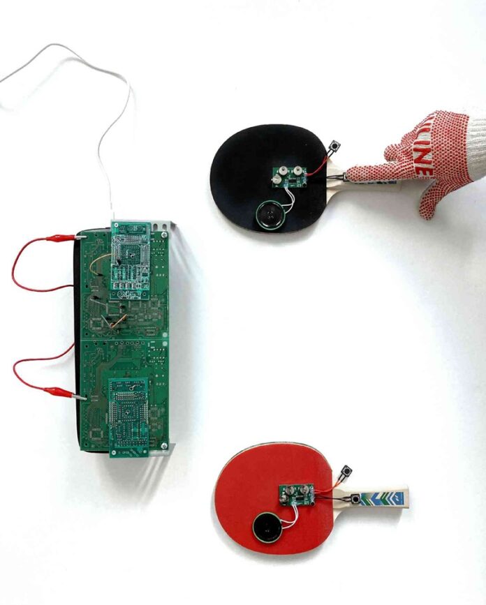 Das Bild zeigt das Ausstellungsplakat. Zu sehen sind zwei Tischtennisschläger, die mit Drähten und akustischen Wiedergabegeräten verbunden sind, sowie eine Halbleitervorrichtung, welche die Kommunikation zwischen beiden Geräten ermöglichen soll. Die soll sinnbildlich für den Austausch zwischen Wien und Tokio stehen.