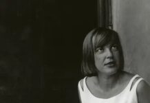 100 Jahre Ingeborg Bachmann / Botschaft Oslo Schwarzweißporträt der Schriftstellerin Ingeborg Bachmann. Sie sitzt seitlich vor einem dunklen Hintergrund und trägt ein ärmelloses, helles Kleid. Ihre Frisur, ein kurzer, glatter Bob umrahmt das Gesicht. Bachmann blickt nach oben rechts außerhalb des Bildausschnitts, ihr Ausdruck wirkt nachdenklich und konzentriert.