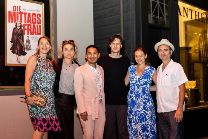 Sandrine Scheller, Marla Emde, Sophoan Soan, Thomas Prenn, Isabella Tomás, Jacques Teisen stehen rechts vor dem Film Plakat von Die Mittags Frau