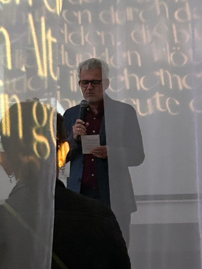 Das Bild zeigt den von Schleiern umgebenen Botschafter beim Lesen eines Trakl-Gedichts