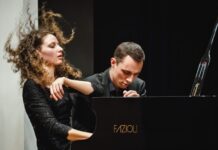 Gugg Piano Duo / Kulturforum New York Das Bild zeigt das Klavierduo The Gugg Piano Duo, bestehend aus Tereza Gugg-Kalabova und Johannes Gugg, während einer intensiven Konzertperformance. Links ist Tereza Gugg-Kalabova zu sehen: Ihr lockiges Haar fliegt in Bewegung nach oben, was die Energie ihres Spiels sichtbar macht. Mit geschlossenen Augen und einem ausdrucksstarken Gesicht wirkt sie ganz in die Musik vertieft. Sie trägt ein elegantes schwarzes Konzertkleid. Rechts sitzt Johannes Gugg am Flügel. Er ist leicht nach vorne geneigt, mit konzentriertem Blick und gespannter Körperhaltung, ganz auf die Ausführung fokussiert. Sein Ausdruck vermittelt Präzision und Hingabe. Beide spielen gemeinsam an einem Konzertflügel und wirken dabei stark aufeinander abgestimmt. Die Szene zeigt eindrucksvoll das Zusammenspiel und die künstlerische Intensität des Duos in einem Moment voller Ausdruck und Dynamik.