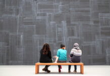 Museum Engagement Strategies / Kulturplattform Arabischer Raum Personen beim Museumsbesuch - man sieht drei Personen von hinten, die auf einer Bank sitzen und auf die Wand vor ihnen schauen
