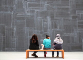 Museum Engagement Strategies / Kulturplattform Arabischer Raum Personen beim Museumsbesuch - man sieht drei Personen von hinten, die auf einer Bank sitzen und auf die Wand vor ihnen schauen