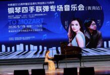 Mitra Kotte & Byron Yue / Kulturform Peking Das Bild zeigt eine Pianistin bei einem Konzert auf einer Bühne in China. Im Hintergrund ist eine große Projektion mit chinesischer Beschriftung zu sehen, die auf ein Klavierkonzert anlässlich des 55-jährigen Jubiläums der diplomatischen Beziehungen zwischen Österreich und China sowie des 270. Geburtstags von Mozart hinweist.