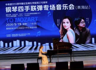 Mitra Kotte & Byron Yue / Kulturform Peking Das Bild zeigt eine Pianistin bei einem Konzert auf einer Bühne in China. Im Hintergrund ist eine große Projektion mit chinesischer Beschriftung zu sehen, die auf ein Klavierkonzert anlässlich des 55-jährigen Jubiläums der diplomatischen Beziehungen zwischen Österreich und China sowie des 270. Geburtstags von Mozart hinweist.