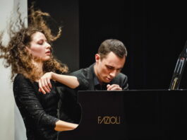 Piano Duo Gugg / Kulturforum Washington Das Bild zeigt das Piano Duo Gugg. Der Musiker sowie die Musikerin sitzen am Flügel und spielen energisch und passioniert darauf.