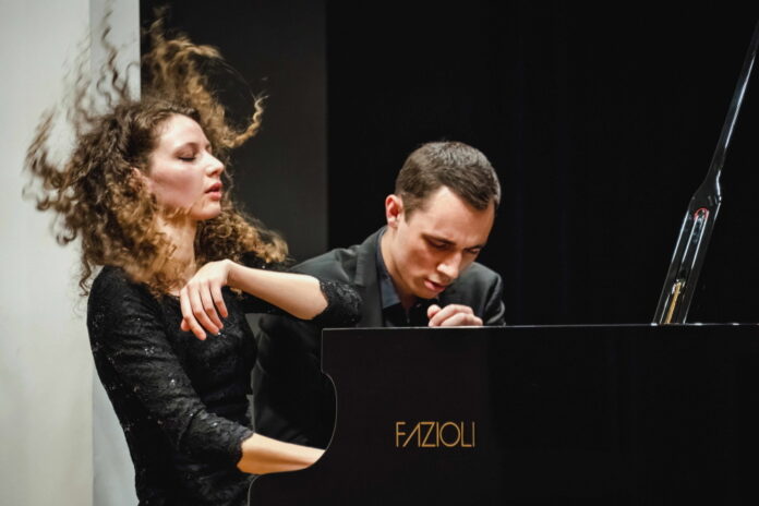 Das Bild zeigt das Piano Duo Gugg. Der Musiker sowie die Musikerin sitzen am Flügel und spielen energisch und passioniert darauf.
