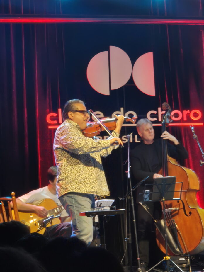 Das Bild zeigt den österreichischen Jazz-Geiger Rudi Berger beim Spiel auf der Bühne des Clube do Choro in Brasília, gemeinsam mit einem brasilianischen Kontrabassisten und einem portugiesischen Gitarristen.