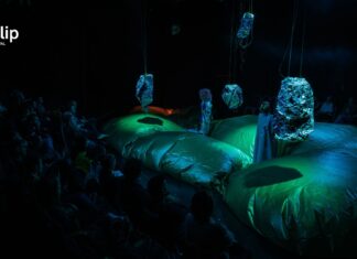 Österreichisches Theater / Botschaft Pristina Das Bild zeigt ein futuristisches Bühnenbild in grün-blau-schwarz mit zwei maskierten Schauspielerinnen.
