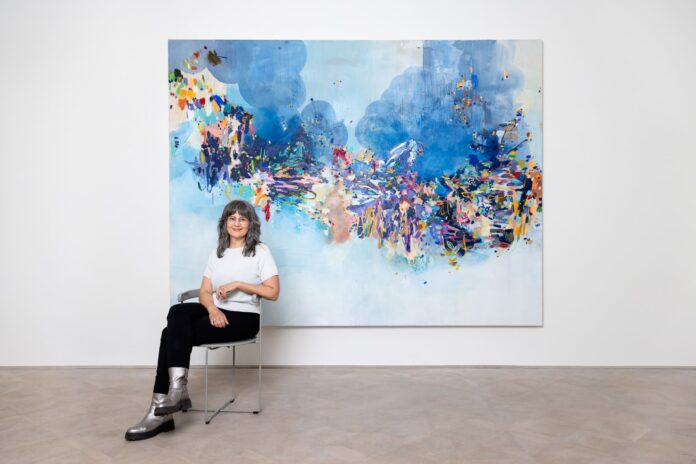 Die Künstlerin Käthe Schönle sitzt vor einem ihrer abstrakten Kunstwerke.