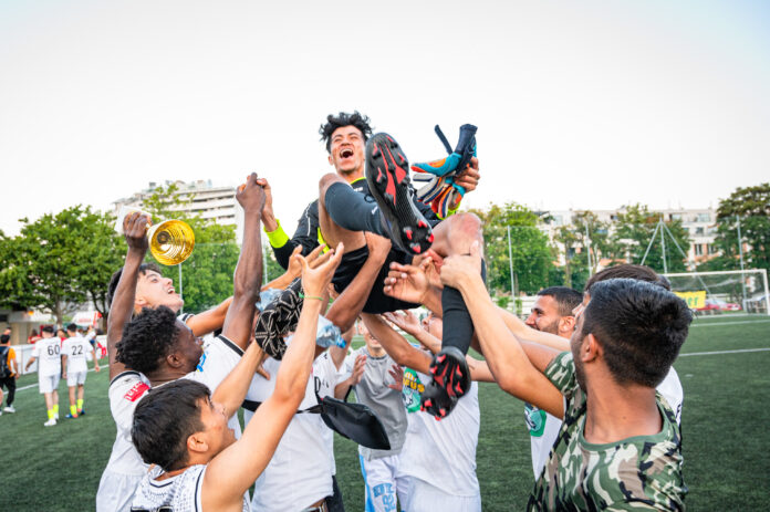 Das Bild zeigt eine Fußballmannschaft, die einen ihrer Spieler in die Höhe hält, ein Spieler hat einen Pokal in der Hand.