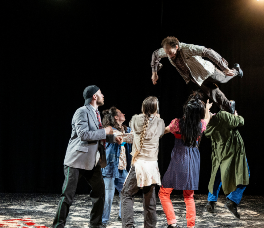 Šibenik Dance Festival / Kulturforum Zagreb Das Bild zeigt eine Tanzgruppe in bunten Kostümen auf der Bühne und eine Person wird in die Luft geworfen.