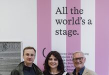 Wolf Suschitzky-Preis 2025 / Podcast WissensART Das Bild zeigt zwei Männer und in der Mitte eine Frau vor einem weiß-rosa gestreiften Plakat