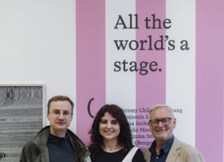Wolf Suschitzky-Preis 2025 / Podcast WissensART Das Bild zeigt zwei Männer und in der Mitte eine Frau vor einem weiß-rosa gestreiften Plakat