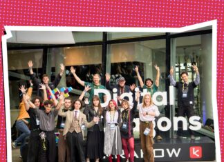 Frau Perchta / Kulturforum Warschau Das Bild zeigt eine Gruppe junger Entwicklerinnen und Entwickler sowie Projektbeteiligte vor dem Eingang von Digital Dragons in Krakau. Die Personen stehen vor dem Logo der Konferenz und winken in die Kamera.