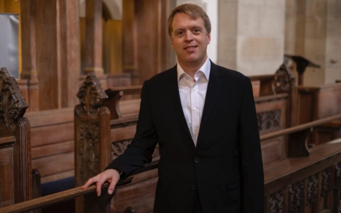 Der Organist Stefan Donner inmitten kunstvoll geschnitzter dunkler Kirchenbänke.