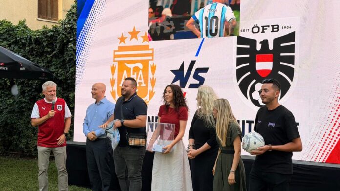 Gruppe von Menschen vor einem LED-Bildschirm mit den Logos der österreichischen und argentinischen Nationalmannschaft.