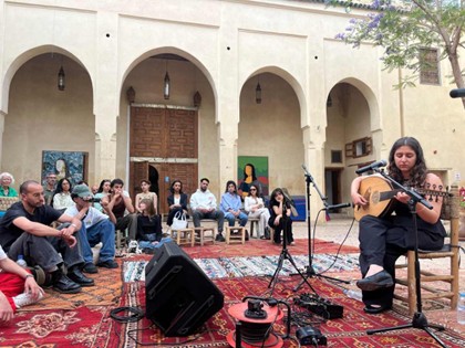 Das Bild zeigt die Musikerin Avin Ahmadi, die vor einem Publikum im Innenhof eines traditionellen marokkanischen Gebäudes Oud spielt