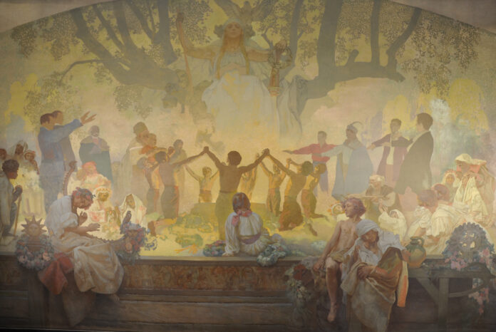 Bild: Alfons Mucha Das Bild zeigt einen Ausschnitt aus dem Malerwerk von Alfons Mucha „Slawisches Epos“. Auf dem Bild, das in gelben Tönen ausgeführt ist, sind mittig halbnackte Männer zu sehen, die in einem Kreis tanzen. Über ihnen sitzt auf einem großen Baum eine slawische Göttin.