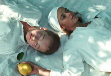 Curtas Vila do Conde / Botschaft Lissabon Filmstill aus „JaneJane Oder das ertrunkene Kind": zwei junge Frauen auf einer Picknickdecke, eine hält eine Quitte in der Hand.