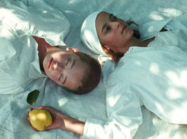 Curtas Vila do Conde / Botschaft Lissabon Filmstill aus „JaneJane Oder das ertrunkene Kind": zwei junge Frauen auf einer Picknickdecke, eine hält eine Quitte in der Hand.
