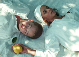 Curtas Vila do Conde / Botschaft Lissabon Filmstill aus „JaneJane Oder das ertrunkene Kind": zwei junge Frauen auf einer Picknickdecke, eine hält eine Quitte in der Hand.