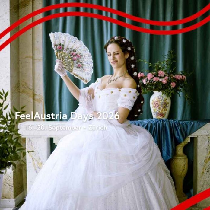 Das Bild ist das Werbemotiv der FeelAustria Days 2026. Zu sehen ist eine moderne Parodie auf Kaiserin Sissi: Eine Person steht in einem weißen, prunkvollen Kleid vor einer kunstvoll gestalteten Kulisse im Barockstil. Sie hält einen Fächer in der Hand und posiert bewusst unkonventionell. Ihr Gesichtsausdruck wirkt lässig und leicht übertrieben, mit einem kleinen, schelmischen Zug, während sie direkt in die Kamera blickt. Im Vordergrund steht in weißer Schrift der Text: „FeelAustria Days 2026 – Von 16. bis 20. September in Zürich“.