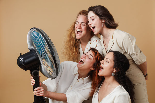 Das Bild zeigt die vier Sängerinnen, eine hält einen kleinen Ventiltor und sie singen in diese Richtung
